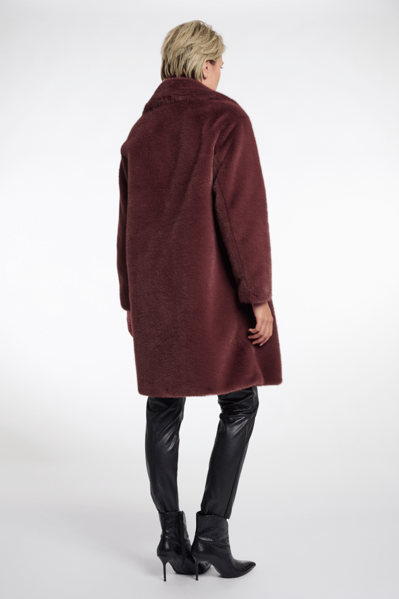 Person wearing a burgundy coat and black leather pants on a white background