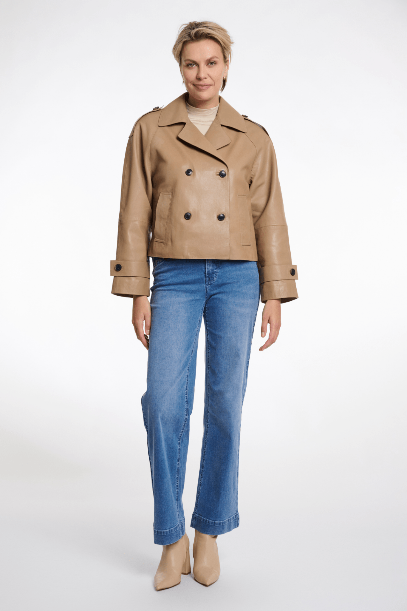 Woman wearing a beige leather jacket and blue jeans on a white background