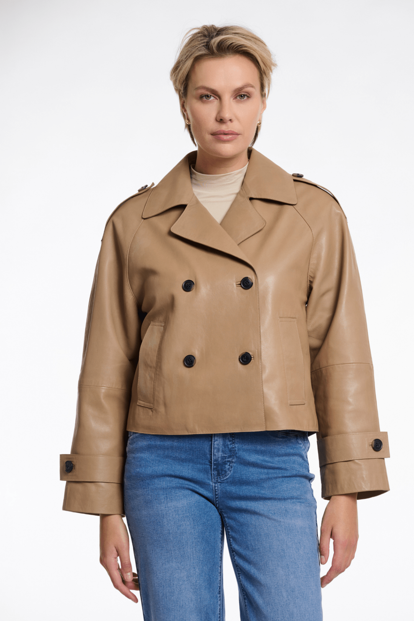Woman wearing a tan leather jacket with black buttons on a white background