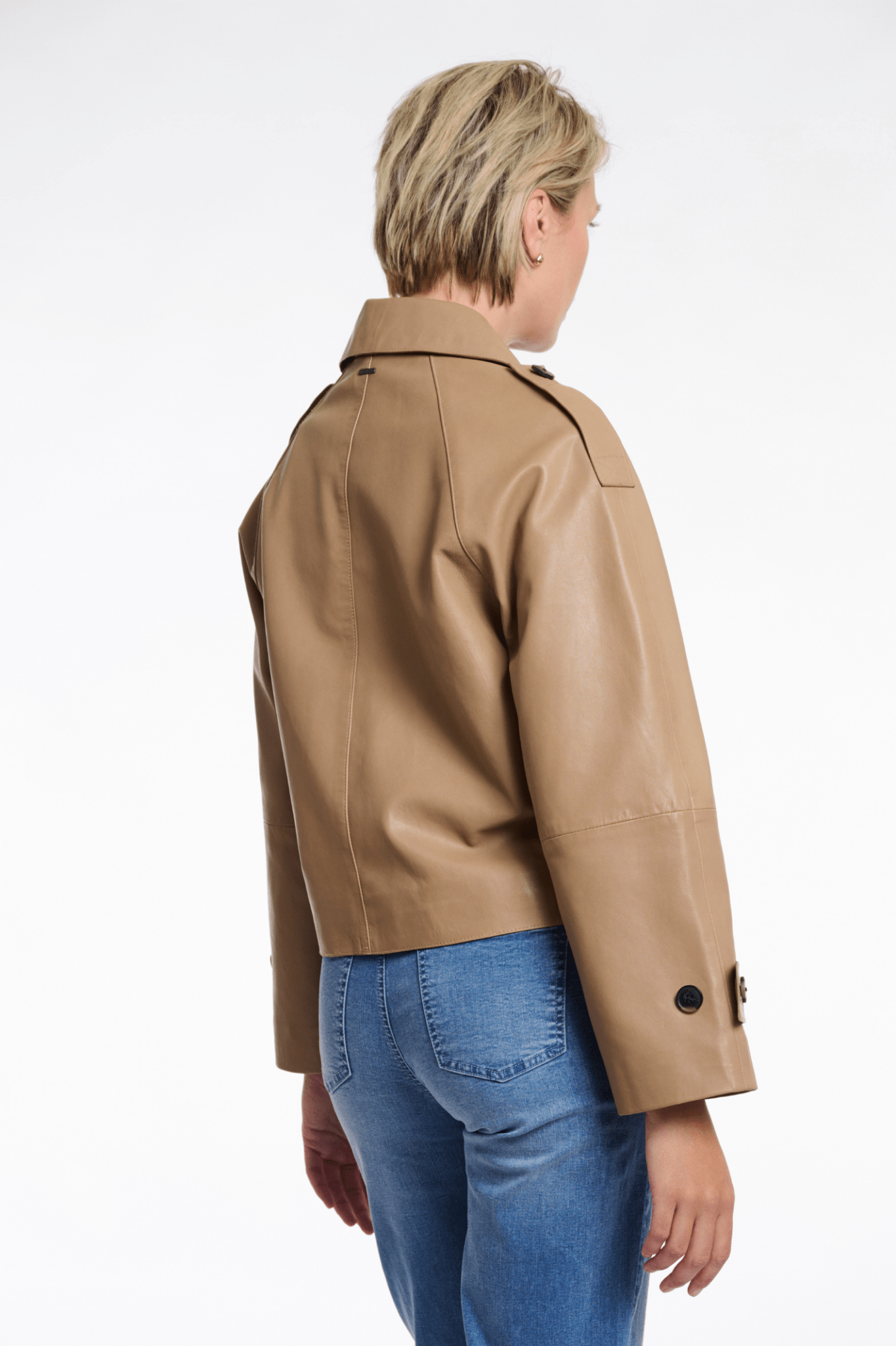 Person wearing a beige leather jacket and blue jeans on a white background