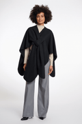 Woman wearing a black poncho over a beige top and gray pants on a white background