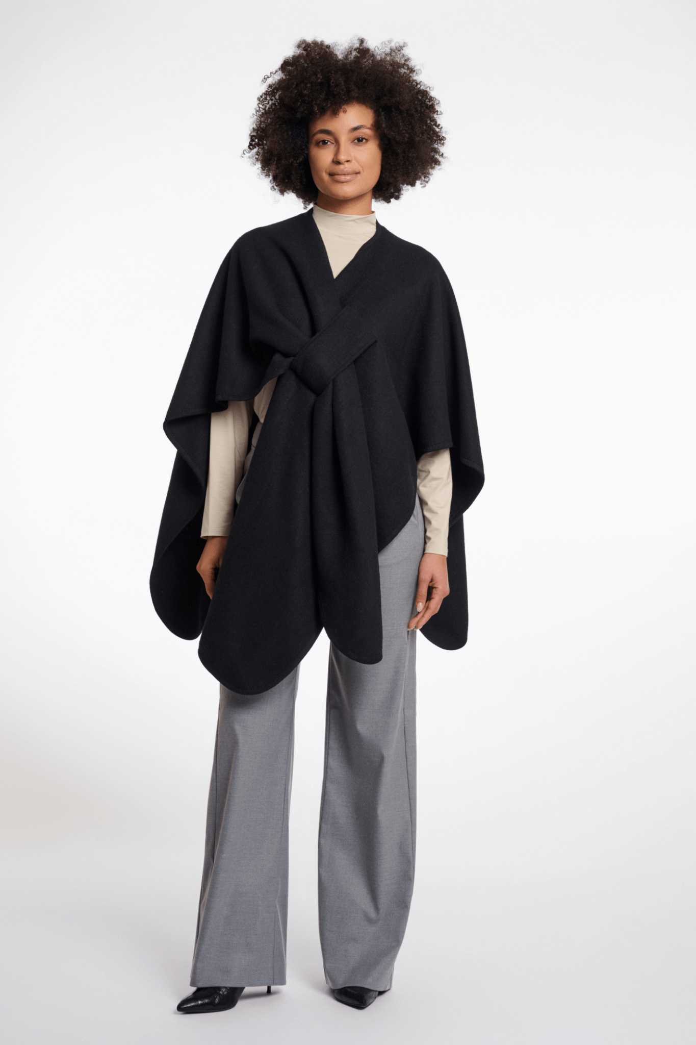 Woman wearing a black poncho over a beige top and gray pants on a white background