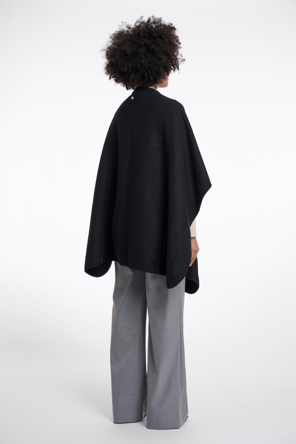 Person wearing a black cape and gray pants on a white background