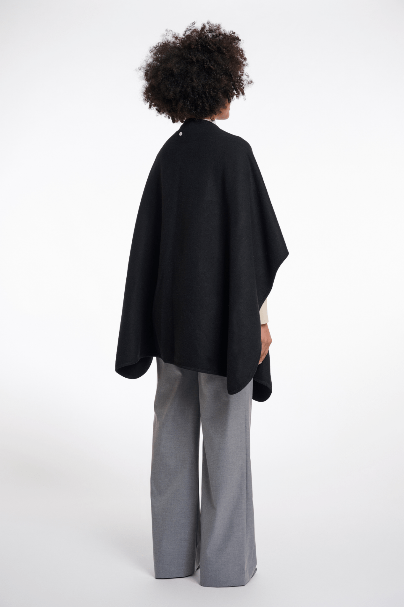 Person wearing a black cape and gray pants on a white background