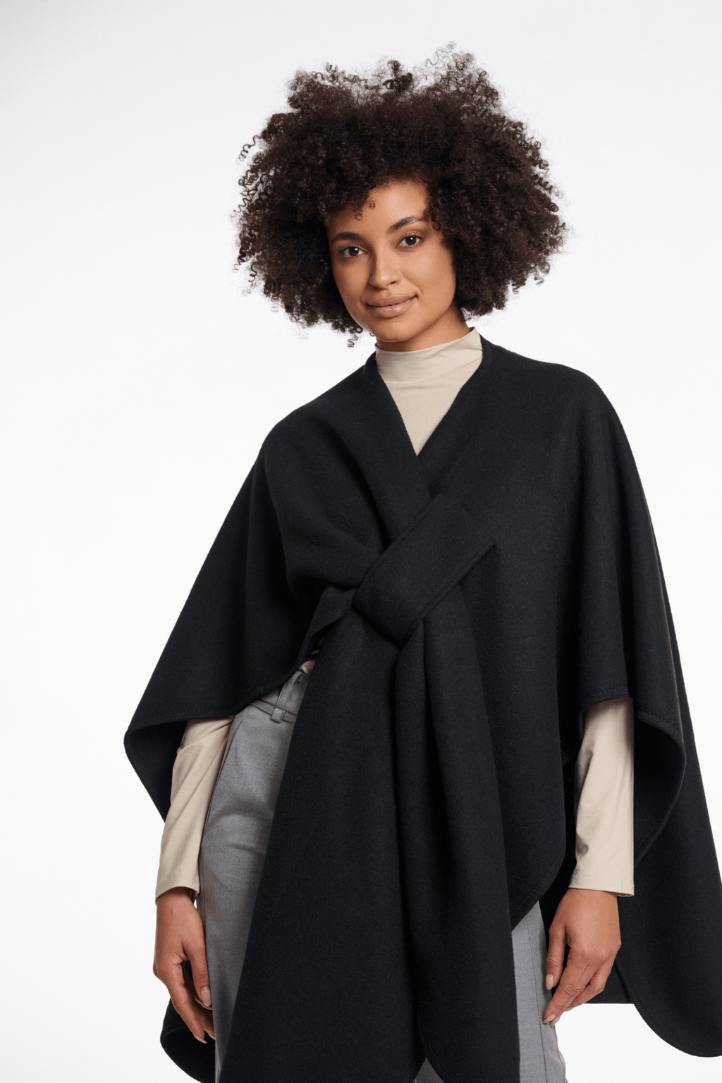 Woman wearing a black poncho over a beige top and gray pants on a white background