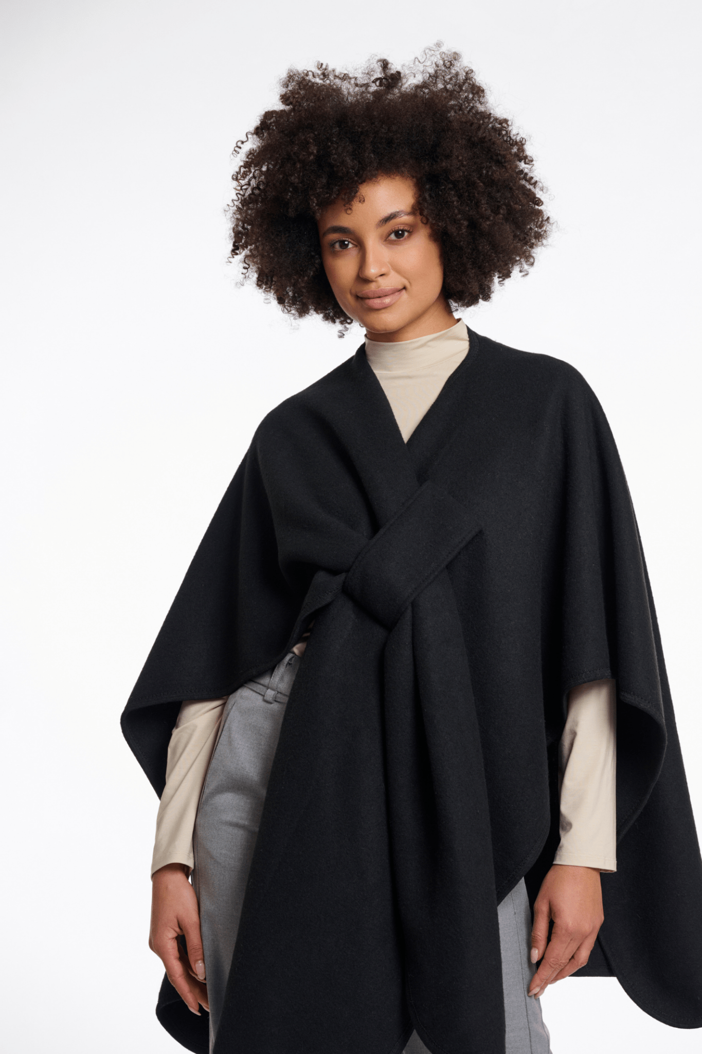 Woman wearing a black poncho over a beige top and gray pants on a white background