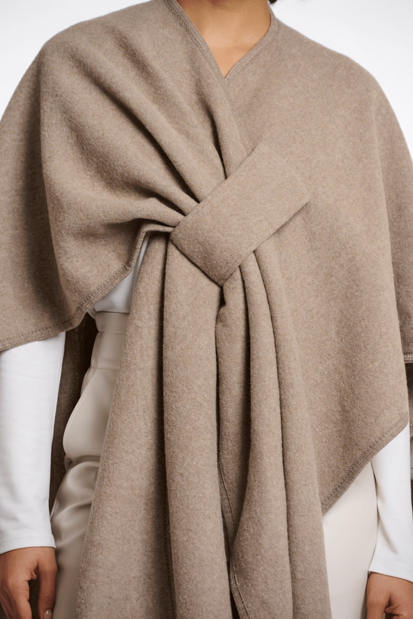 Beige poncho being worn by a person on a white background