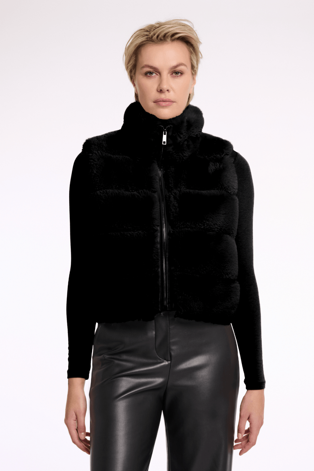 Woman wearing a black puffer vest over a black top with leather pants on a white background