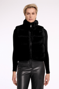 Woman wearing a black puffer vest over a black top with leather pants on a white background