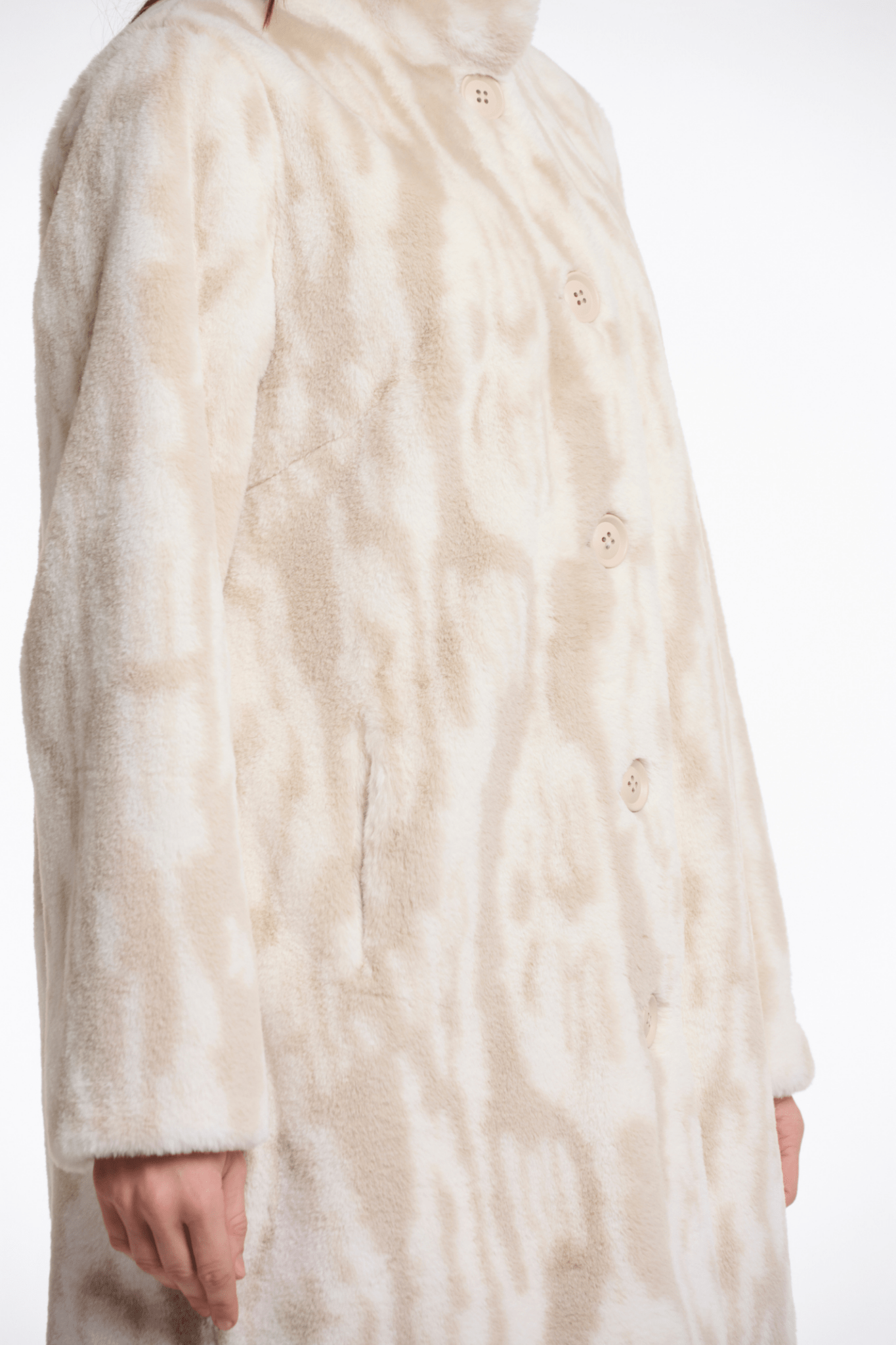 Close-up of a person wearing a long, light-colored fur coat on a white background