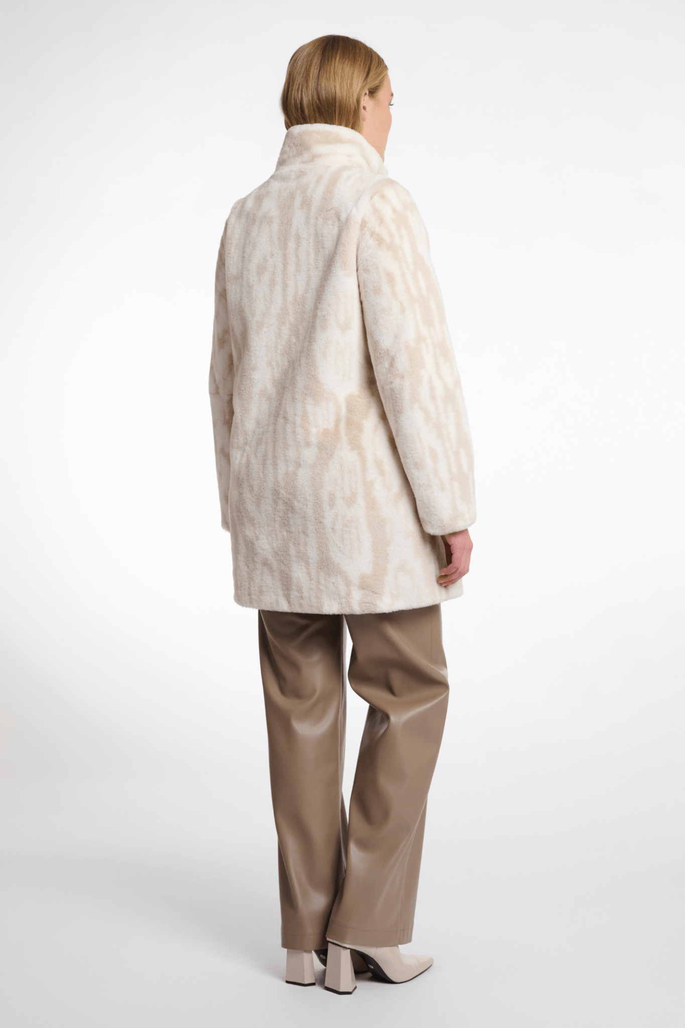 Person wearing a cream-colored coat and beige pants on a white background