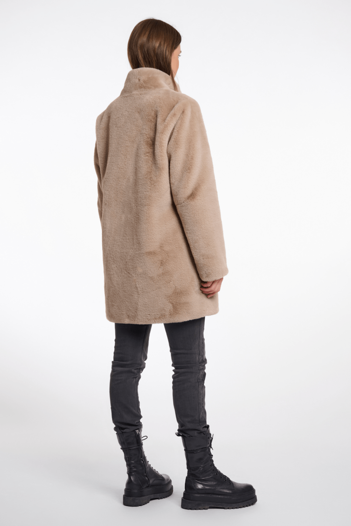 Person wearing a beige coat, black pants, and black boots on a white background