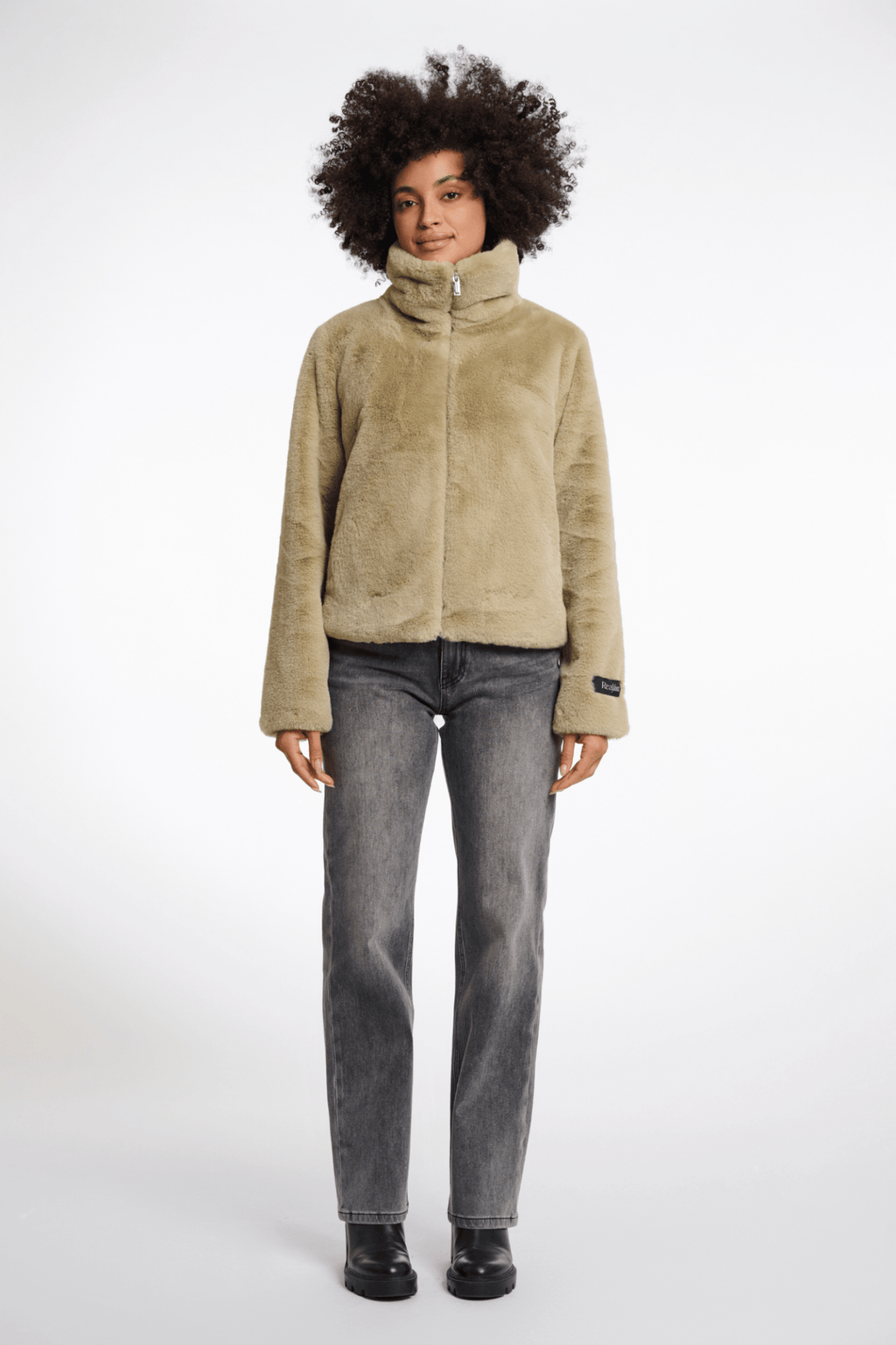 Person wearing a beige fleece jacket and gray jeans on a white background