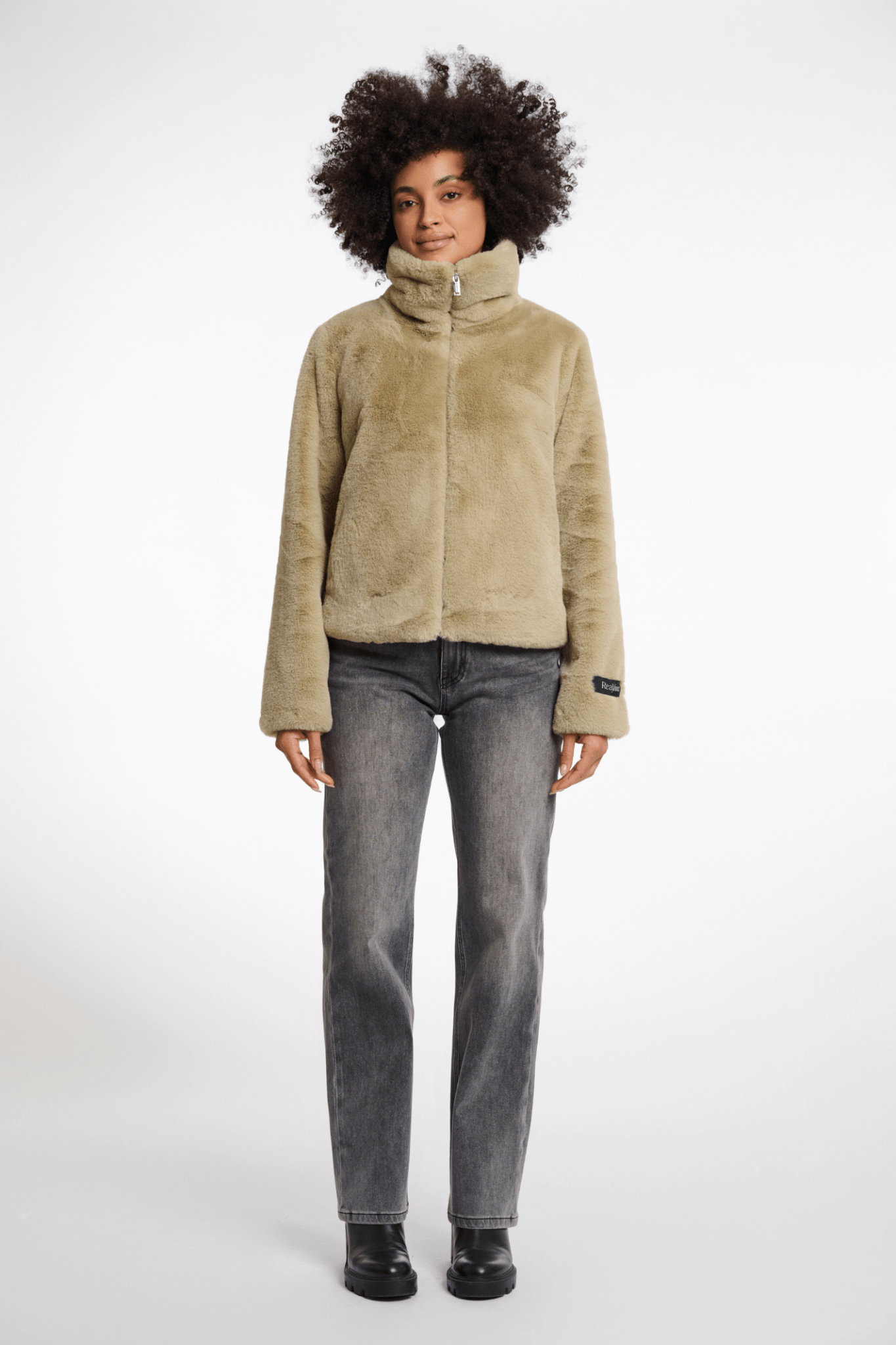 Person wearing a beige fleece jacket and gray jeans on a white background