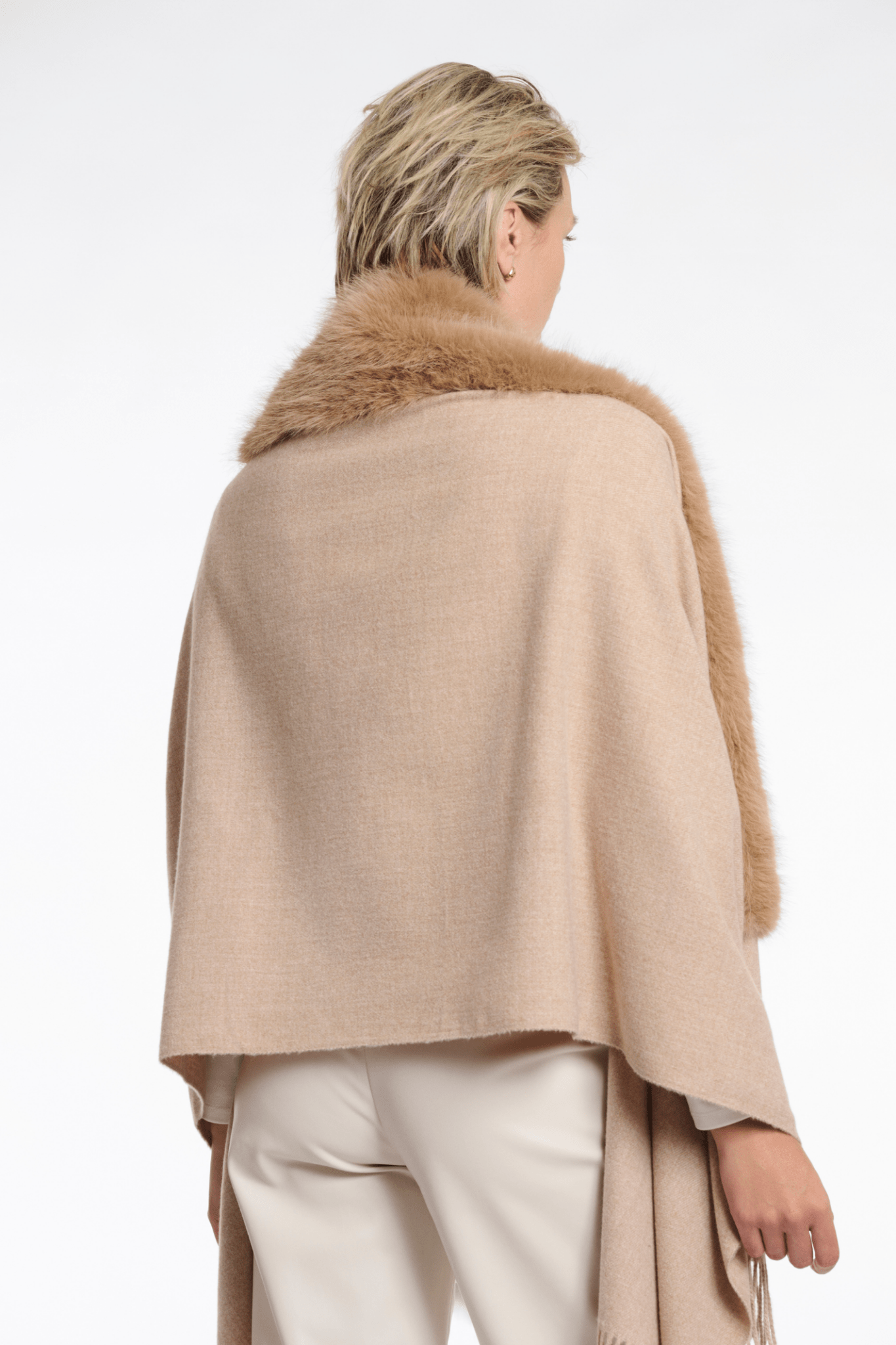 Person wearing a beige poncho with fur collar on a white background