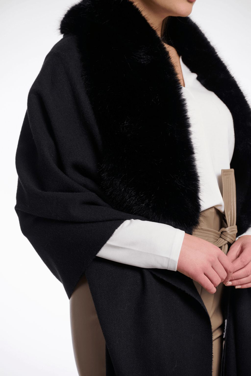Black fur-trimmed coat with a white shirt and beige pants on a white background