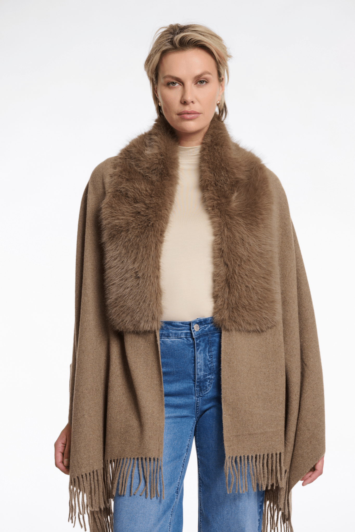 Woman wearing a brown fur-trimmed poncho with blue jeans on a white background