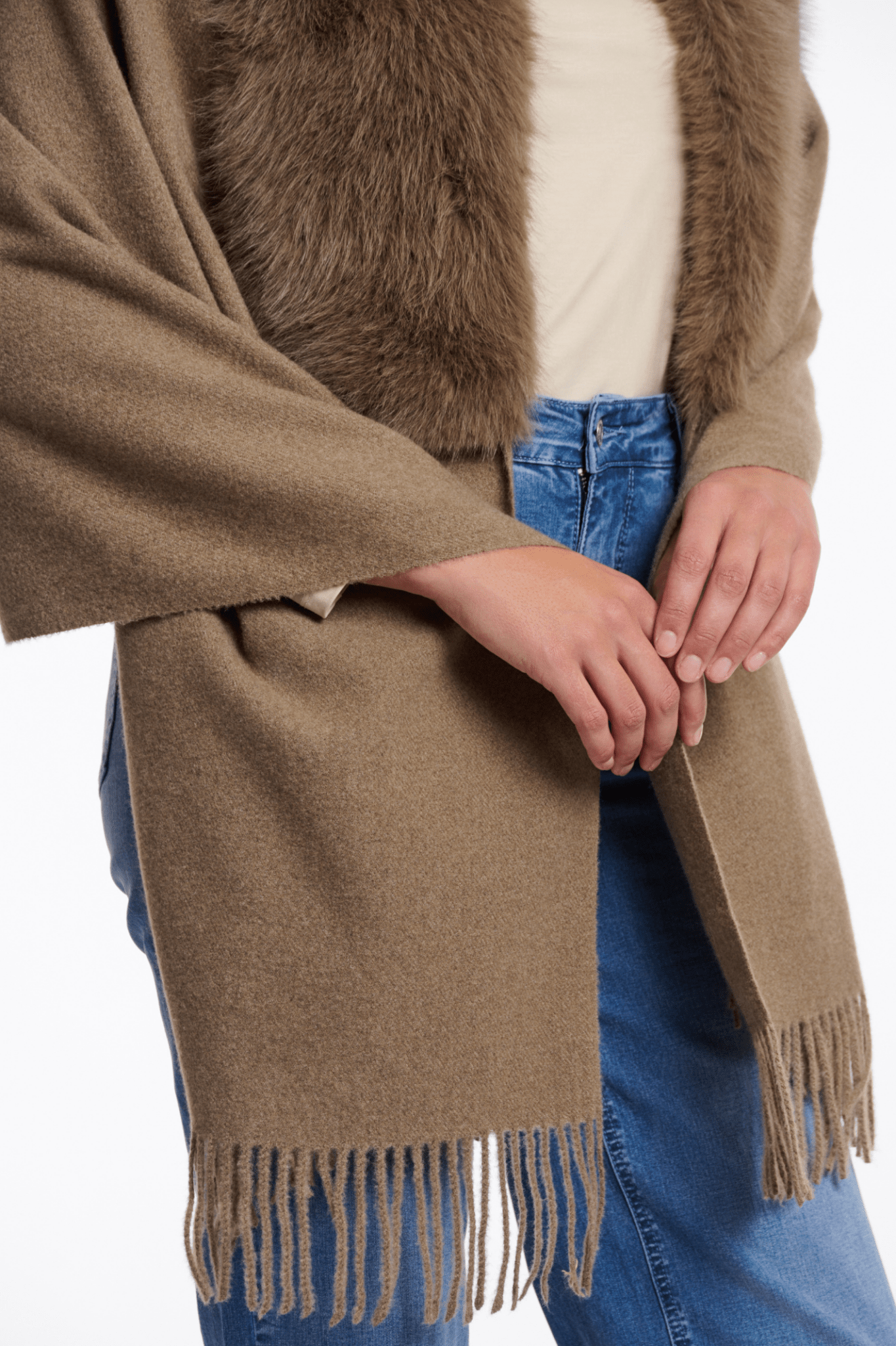 Person wearing a brown fringed scarf with a neutral background