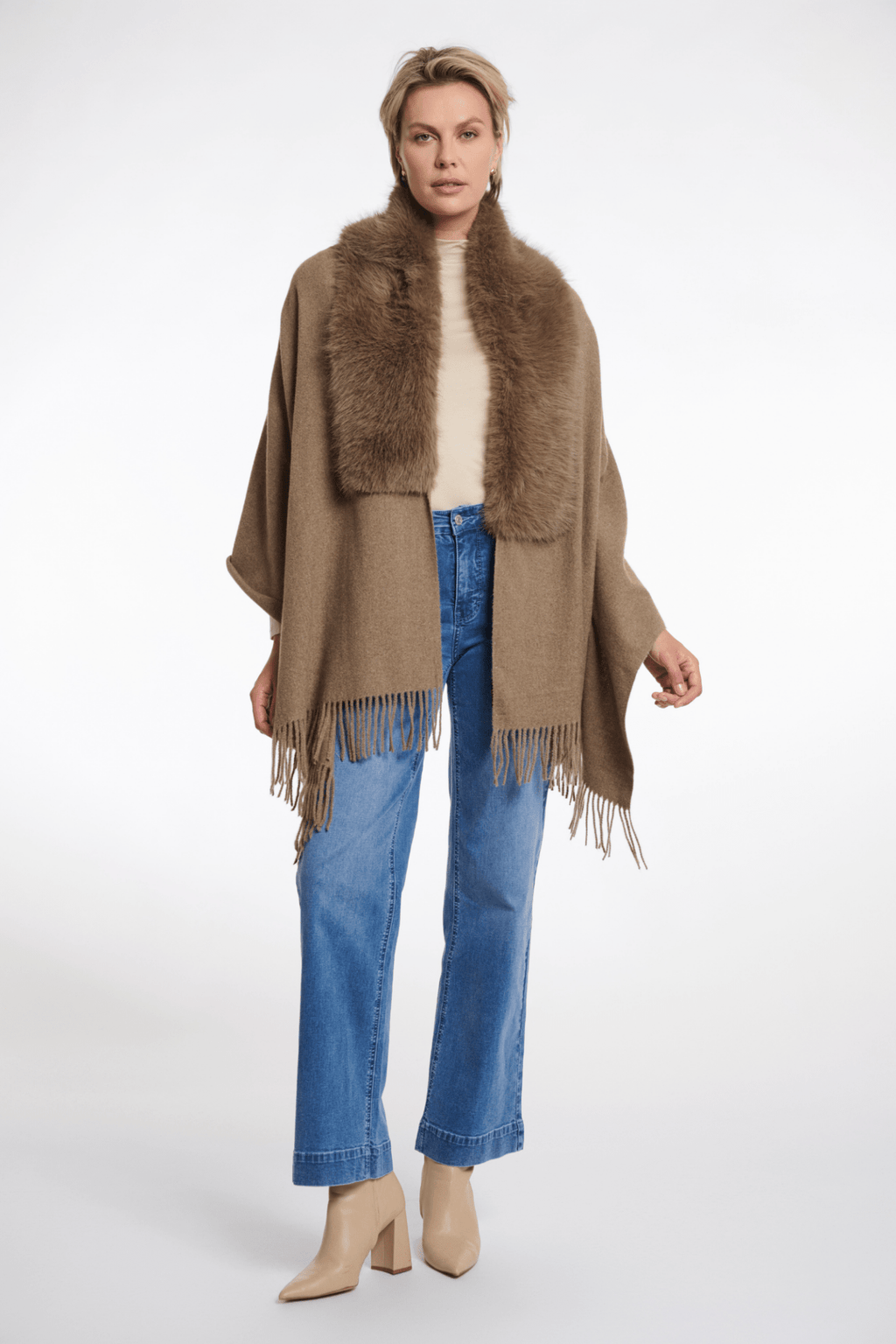 Woman wearing a brown poncho with fur collar and blue jeans on a white background