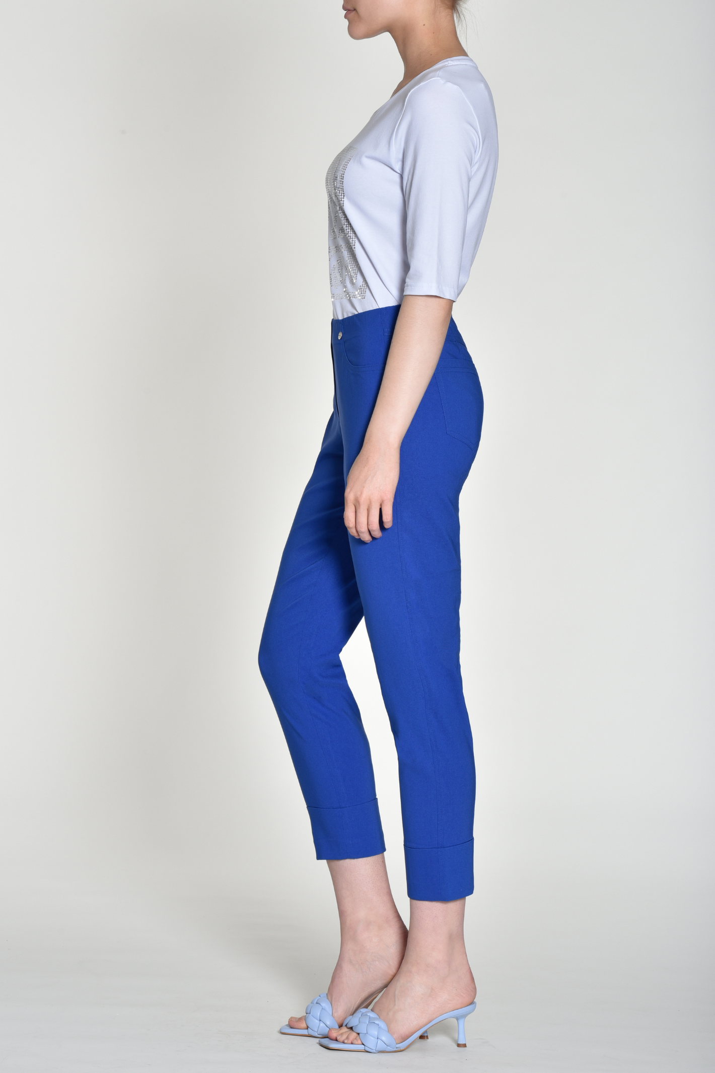 Side view of woman wearing royal blue slim-fit cropped trousers with cuffed hems and high waist on light background